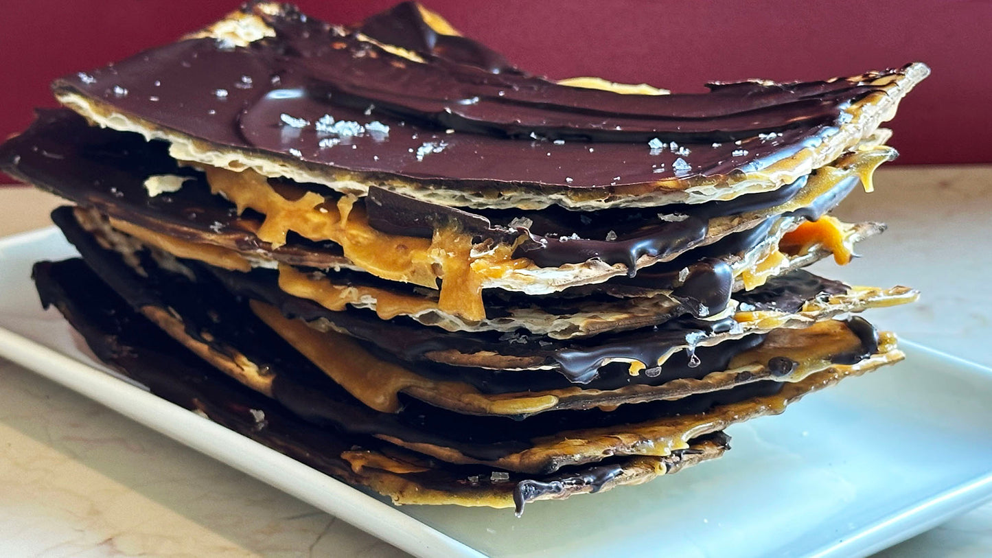 A stack of chocolate, caramel matzoh sprinkled with sea salt on a rectangular white plate - yum