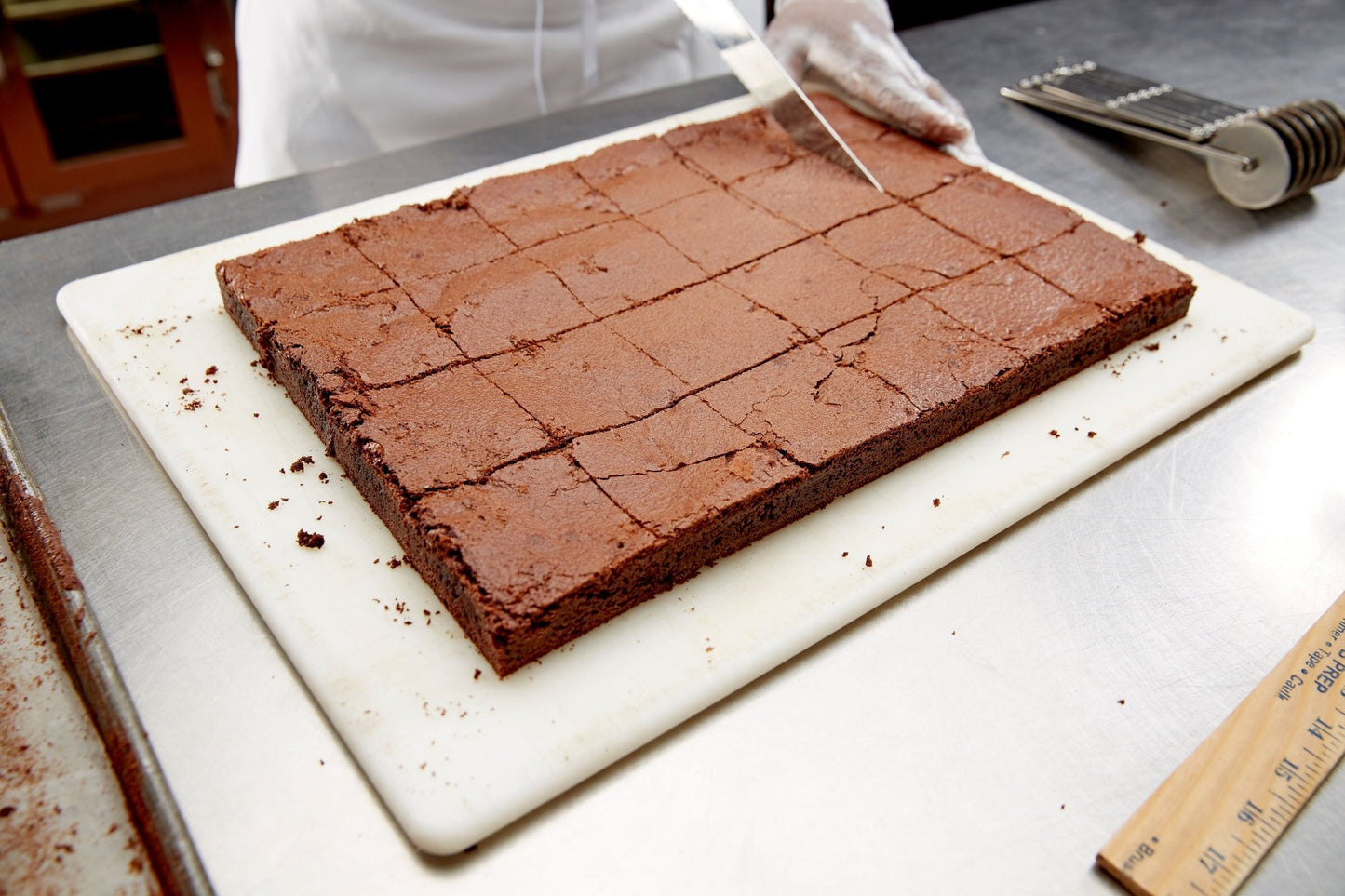 
                  
                    A chef cutting a tray of brownies. ruler and scoring tool on the stainless steel counter
                  
                